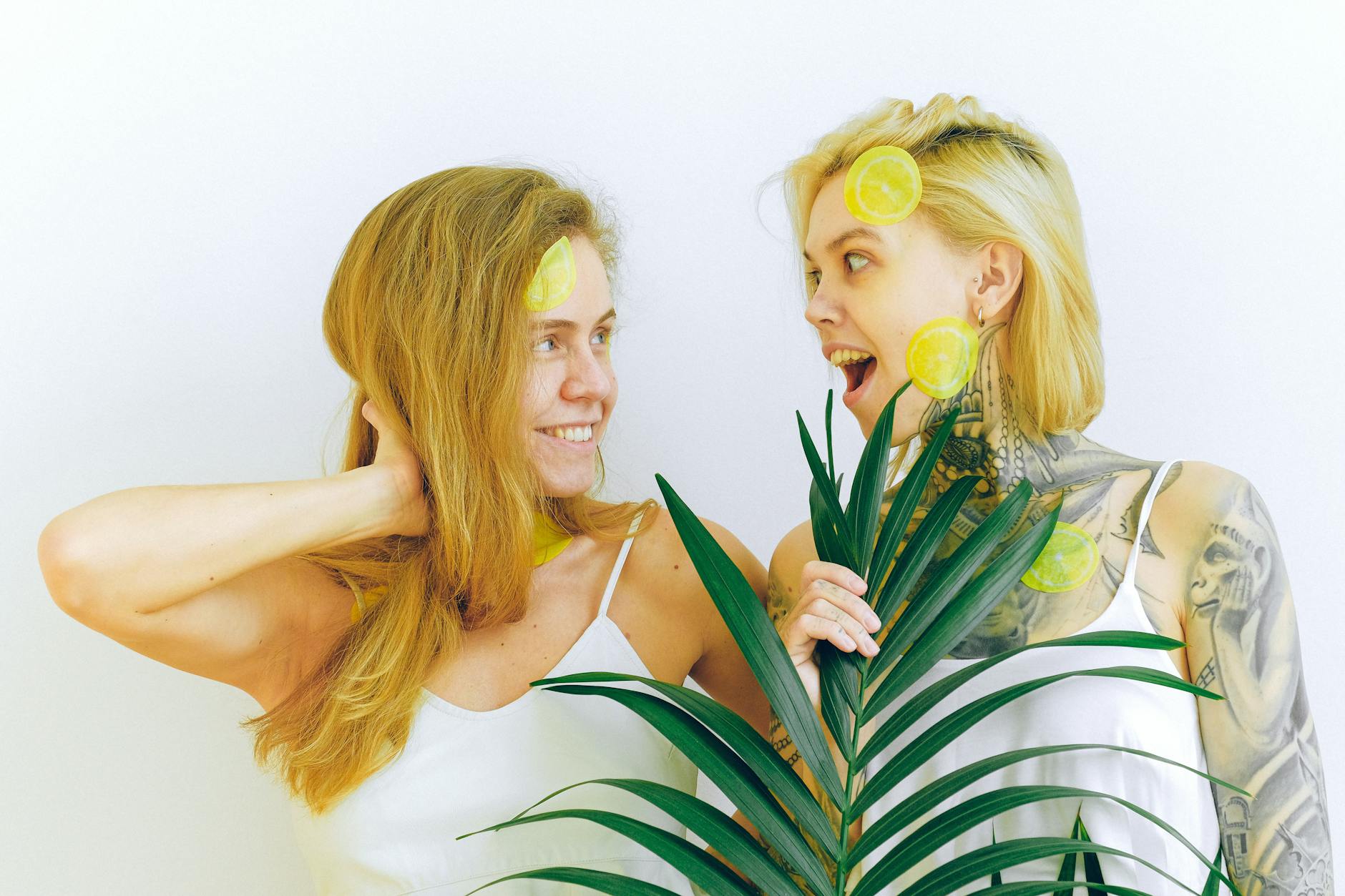 Two women smiling with tropical plants indoors, conveying comfort and ease