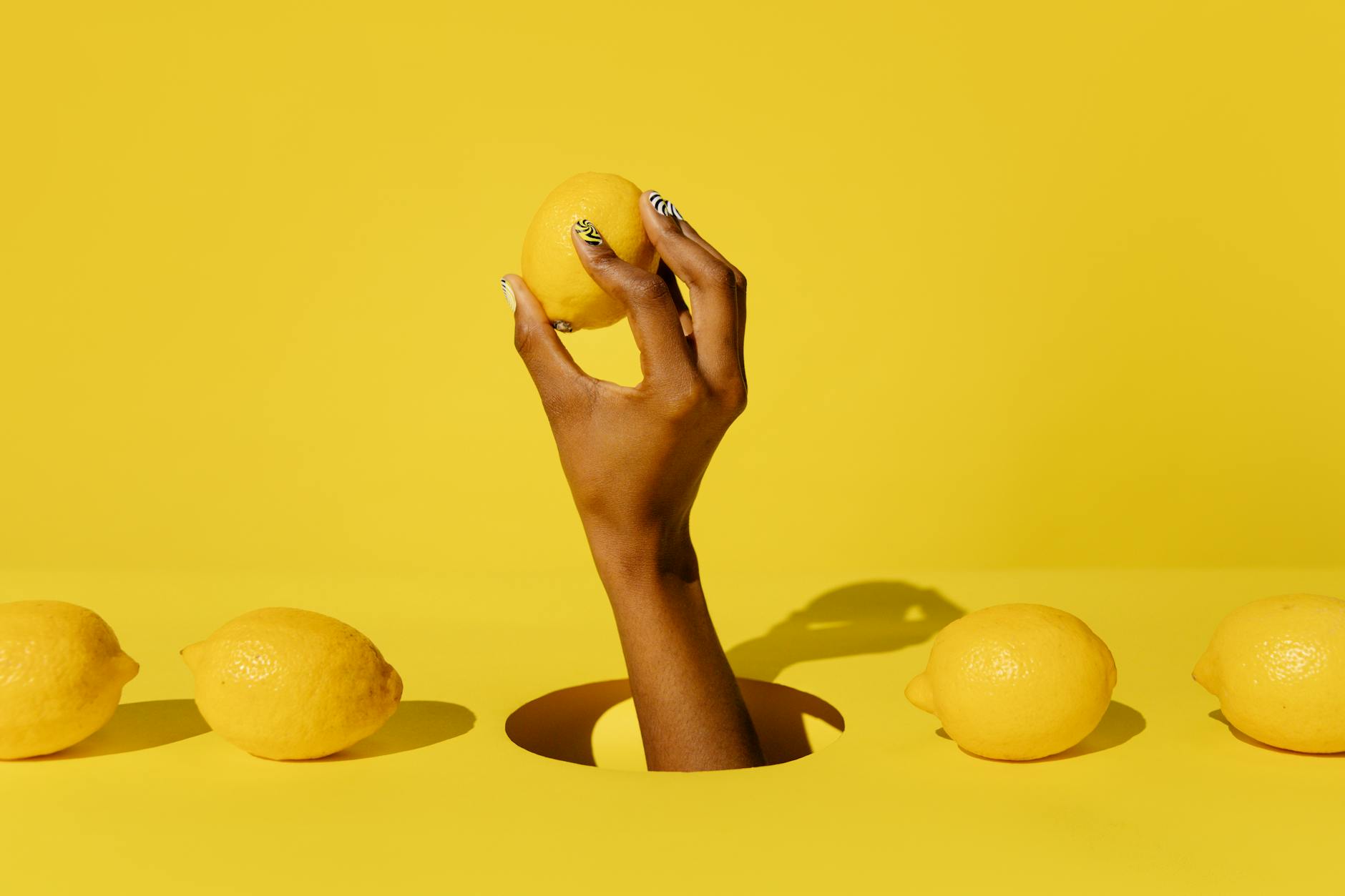 A hand holding a lemon against a bright yellow background, representing gentle, fresh stimulation for sensitive healing