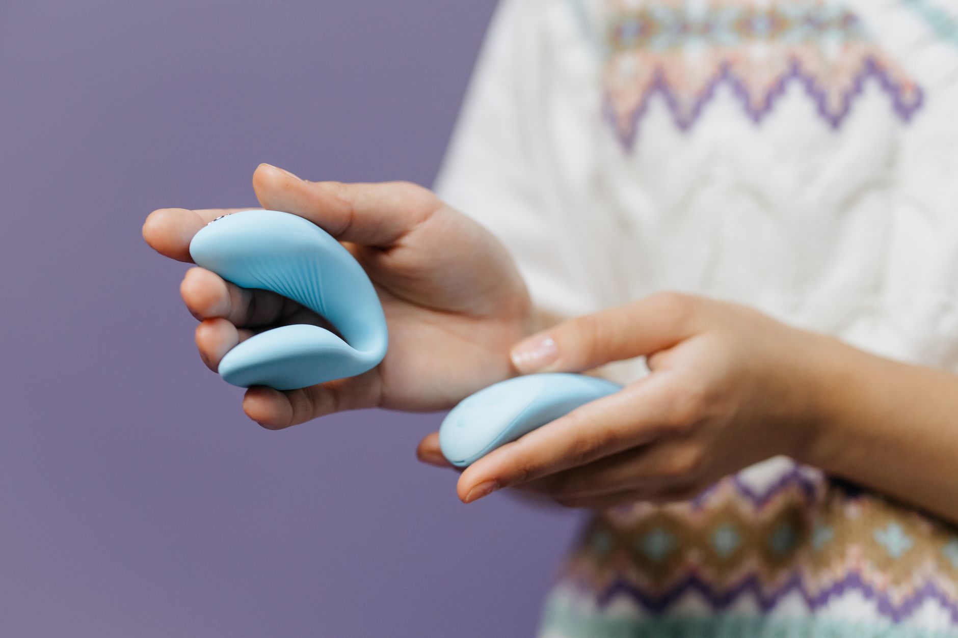Close-up of hands holding a sleek blue vibrator against a purple background, showcasing the design of a modern suction toy.