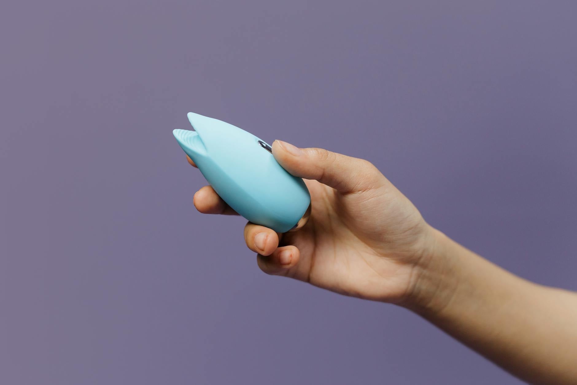A blue silicone clitoral vibrator held against a purple background