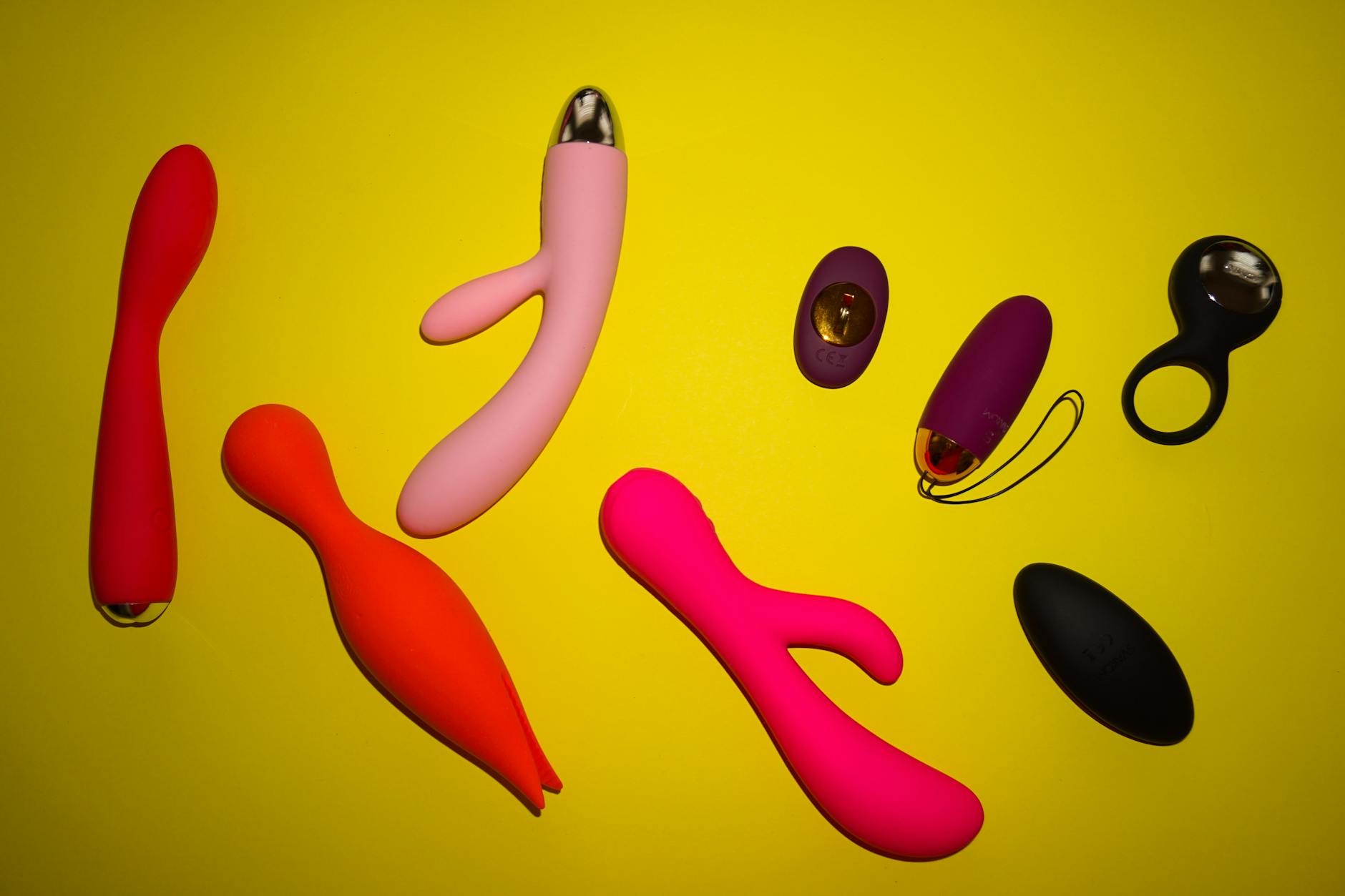 Variety of colorful sex toys displayed on a bright yellow surface showing different shapes and designs